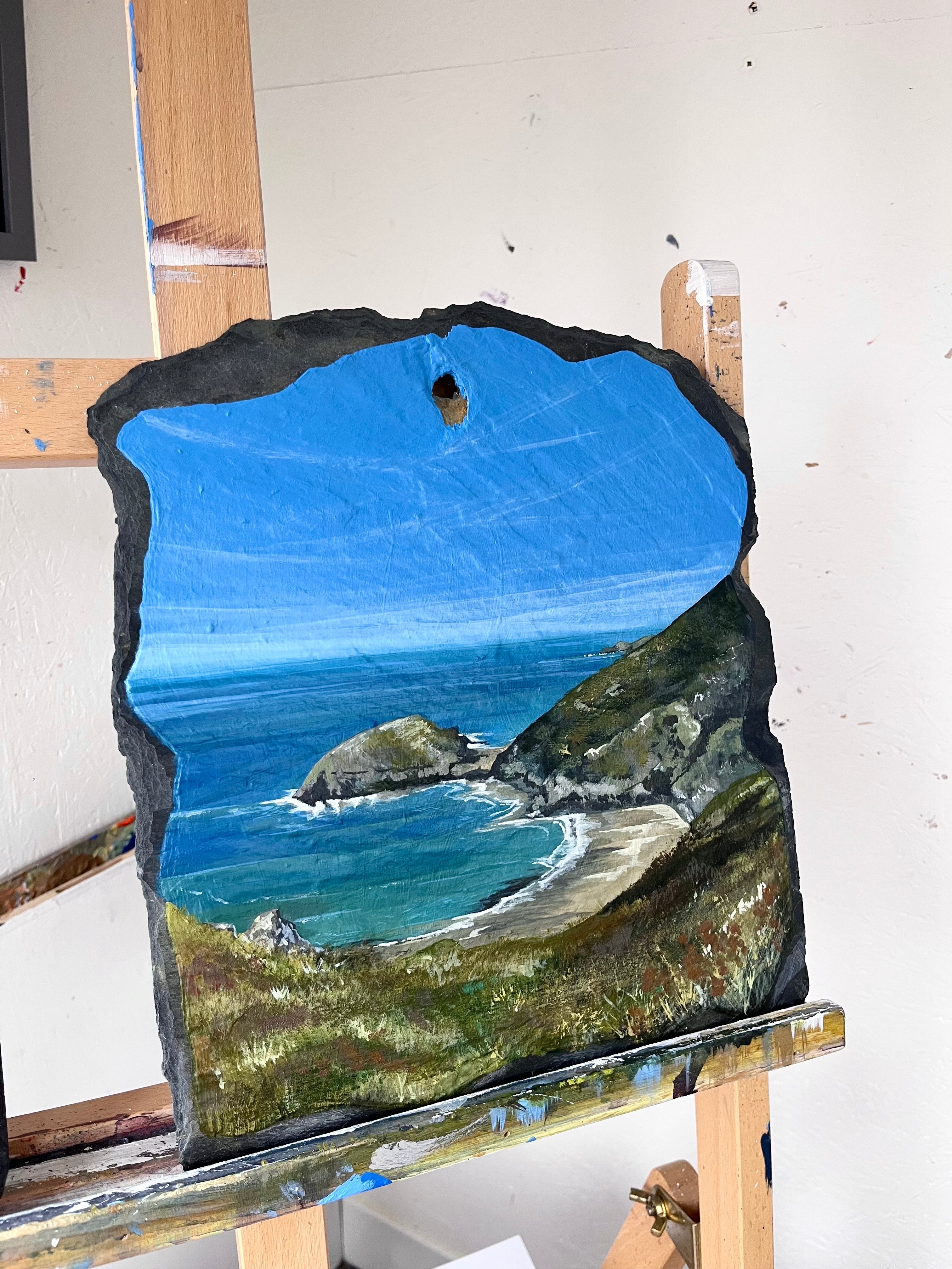 Artistic depiction of a coastal scene on a rock with blue sky and ocean.