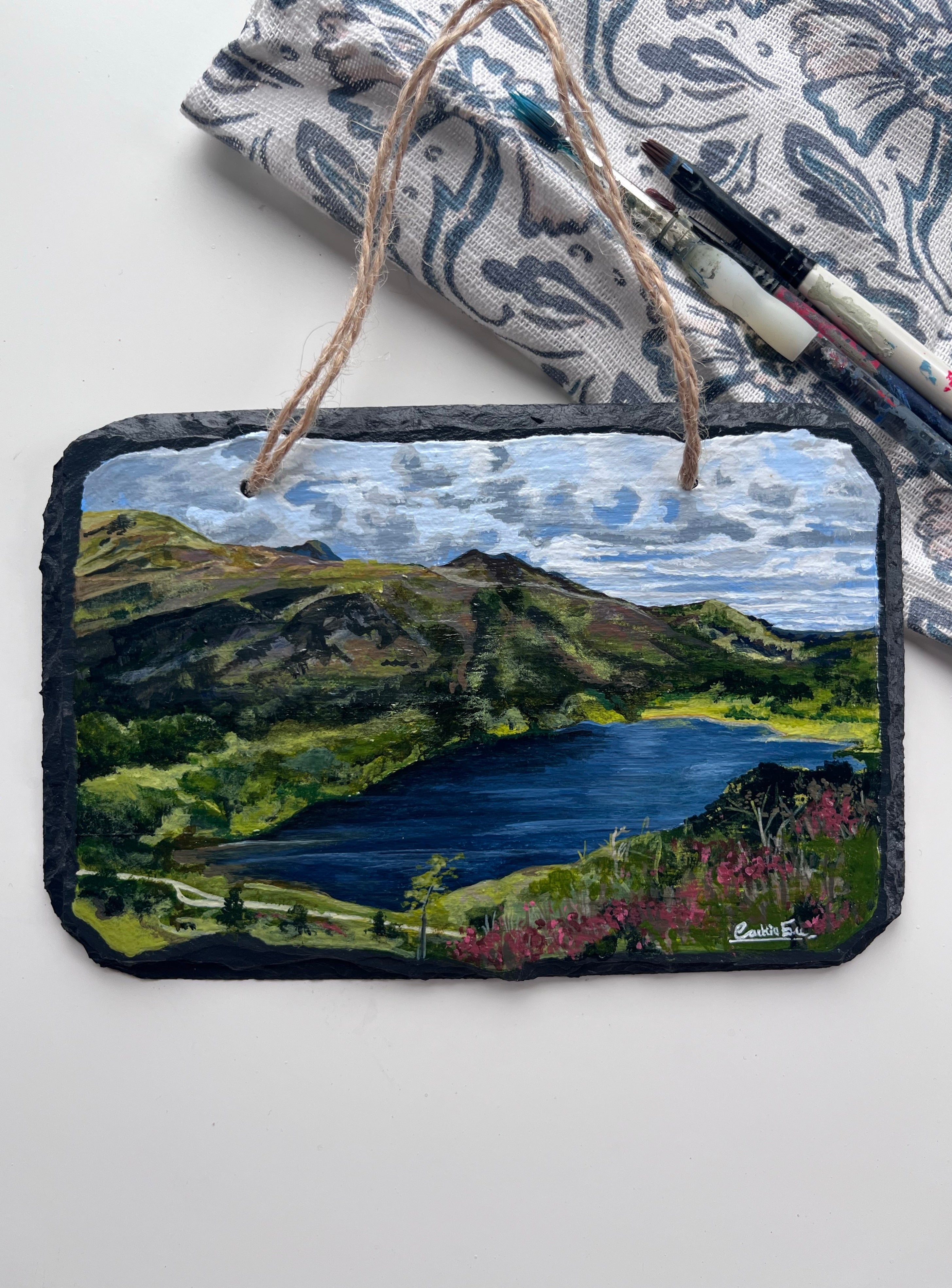 Decorative slate with a mountain lake painting, tied with twine, on a white background.